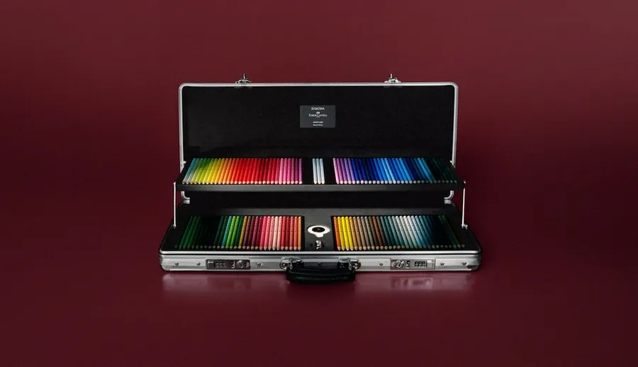 Der Artist Case von RIMOWA × Faber-Castell, geöffnet vor dunkelrotem Hintergrund, beide Einsätze voller Farbstifte